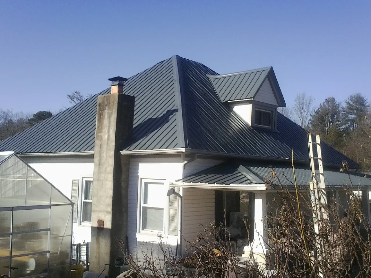 Dark blue standing seam metal roof on a white farmhouse with dormer — Slate & Tile Roof Repair by Roofing Brothers in Manilla