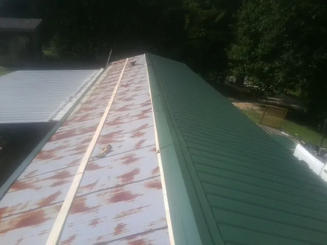 Old rusted panels beside newly installed green metal roofing — Wind Damage Roof Repair by Roofing Brothers in Manilla