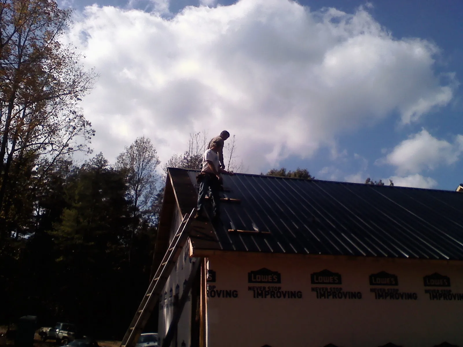 Roofer fastening dark metal panels high against a cloudy sky, from a Roof Inspection job in Manilla