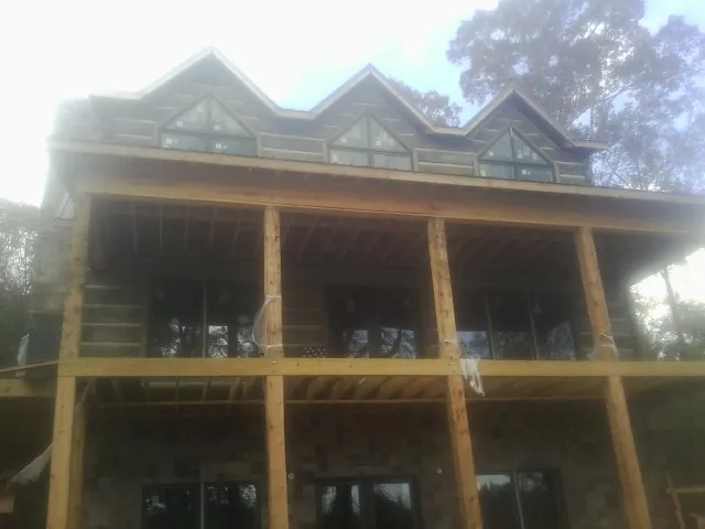 Dormers and porch framing on a large log home under construction — Roof Coating work by our crew in Manilla