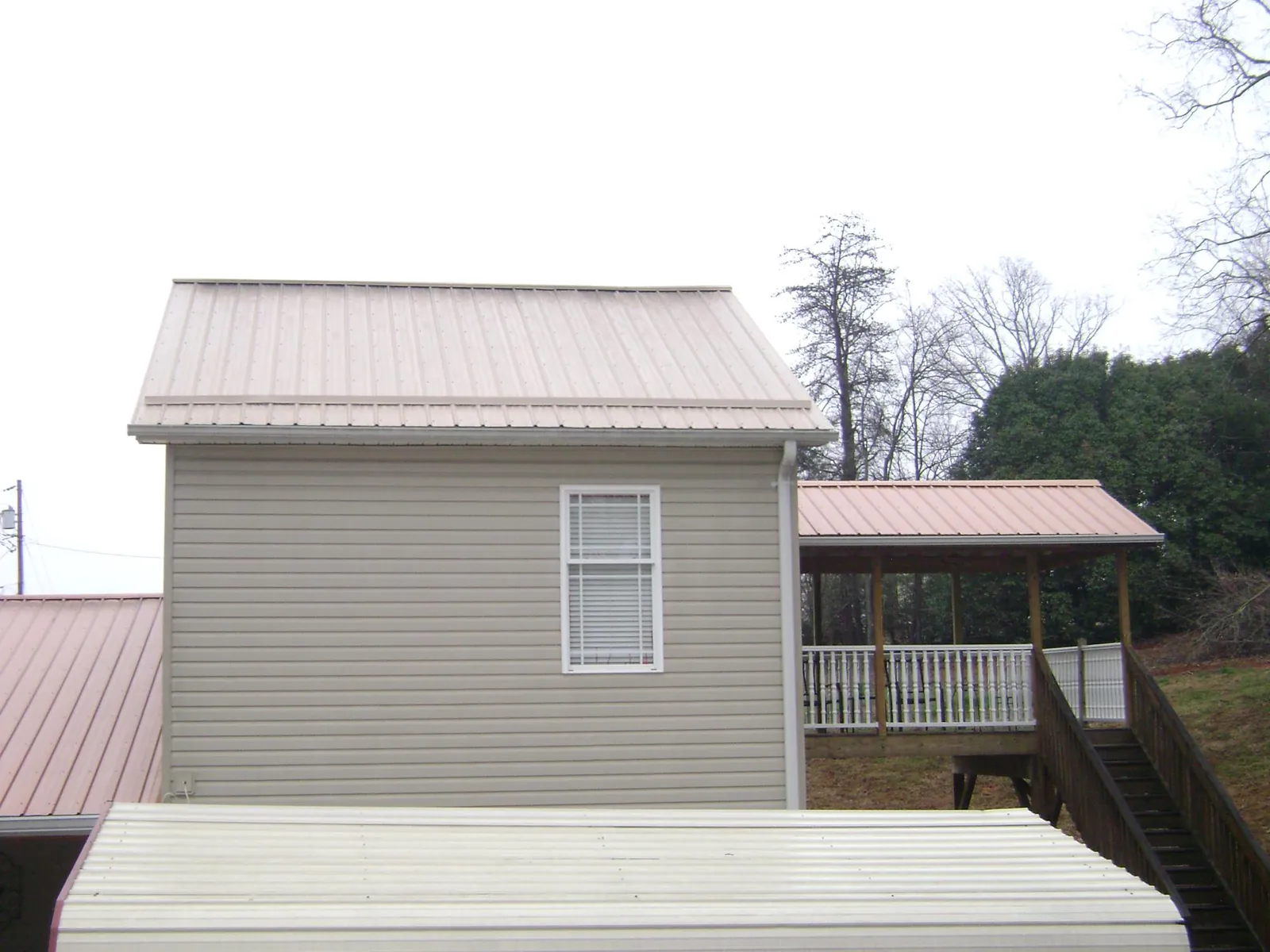 Tan metal roofs on a two story addition and attached porch, from a Roof Replacement job in Manilla