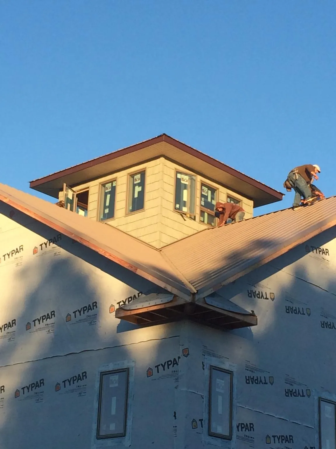 Roofers working around a rooftop cupola on a new metal roof at sunset — Roof Waterproofing in Manilla by Roofing Brothers